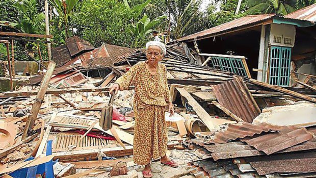 Ibu Mariani, 75, finds her handbag in the ruins of her home.