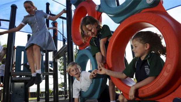Burgmann Anglican students (foreground, from left) Lachlan Furini, Alison Riley and Kate Riley play on yard equipment after school.