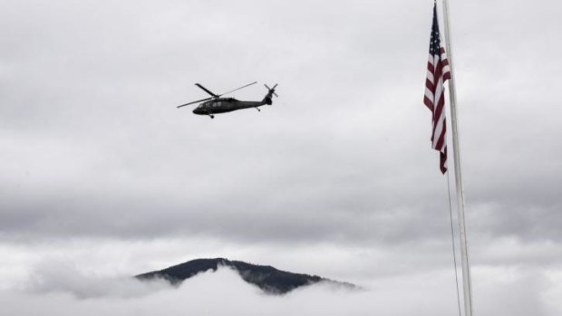 A military helicopter flying to the site of a massive mudslide passes by a flag set at half staff in Darrington, Washington. 