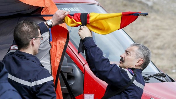 French firefighters tie a black ribbon to  a Spanish flag outside a tent where relatives and officials are due to pay tribute to the victims of the Airbus A320 crash.