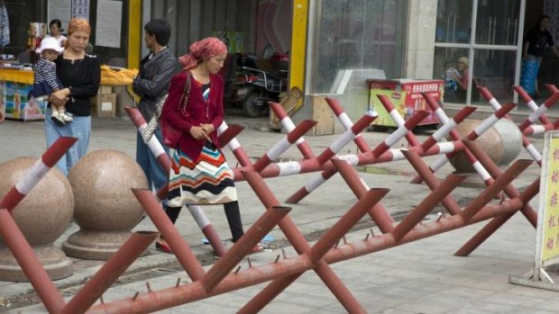 Tightened grip: Uighur women walk past barricades at the entrance to a shopping district in the city of Aksu, Xinjiang province.