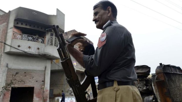 A Pakistani policeman slings his weapon as he stands guard outside the smoke-charred house of an Ahmadi Muslim resident following an attack by an angry mob.