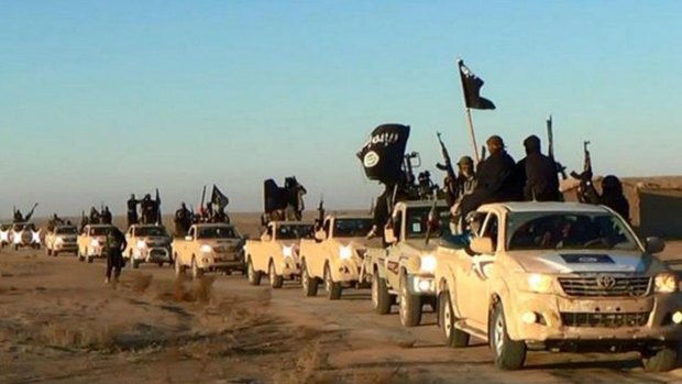 Islamic State militants hold up their weapons and wave the group's flags on their vehicles in a convoy in Raqqa, Syria.