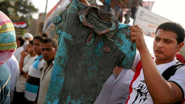 A man holds up a bloodied shirt  at a pro-Mohamed Mursi rally near where over 50 were purported to have been killed.