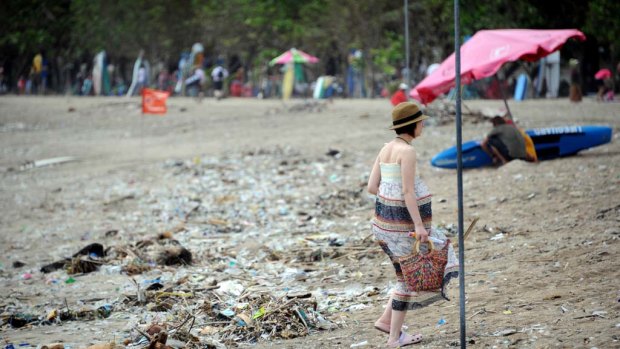 A foreign tourist  walks past debris and rubbish at  Kuta Beach.