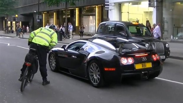 A policeman on a bicycle questions the driver of a Bugatti Veyron.