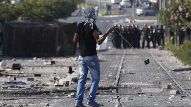 A Palestinian throws stones towards Israeli police.