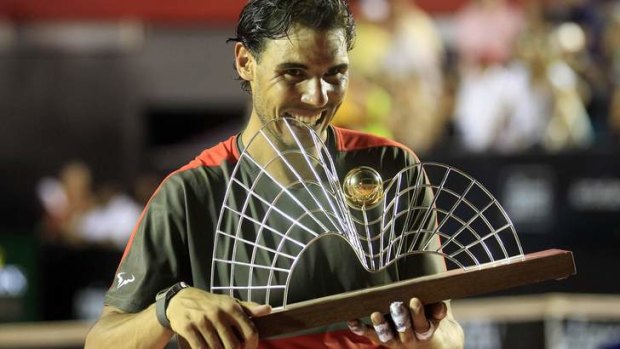 Rafael Nadal bites his trophy after winning against Alexandr Dolgopolov at the 2014 Rio Open men's final.