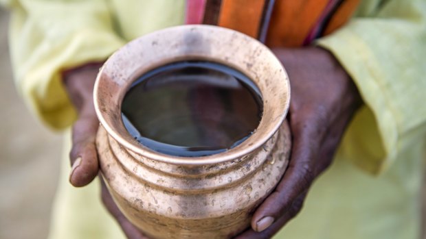 A local holds a cup of well water in Haryana, India.
