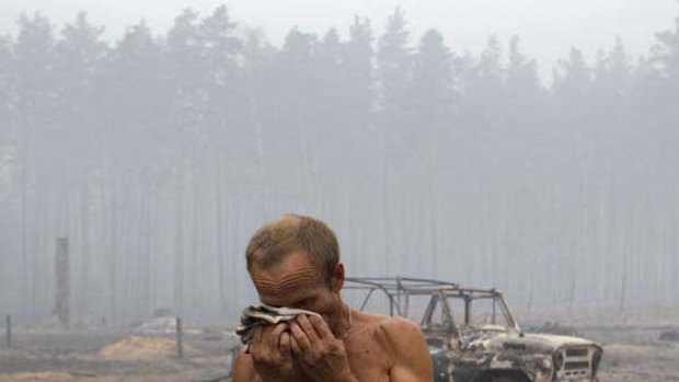 Alexander, 50, wipes his face in front of a charred car during a fire at the village of Peredeltsy that was burned to the ground by a wildfire in Ryazan region. <i>Picture: AP/Sergey Ponomarev</i>