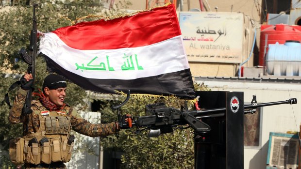 An Iraqi armed soldier waves an Iraqi flag in Baghdad to celebrate the victory of the Iraqi National Football team over Iran in Canberra