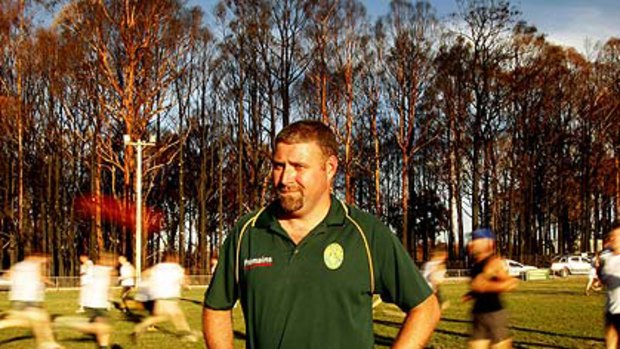 Cameron Caine, President of the Kinglake Football Club, stands on Memorial Oval as players perform training drills on the ground.