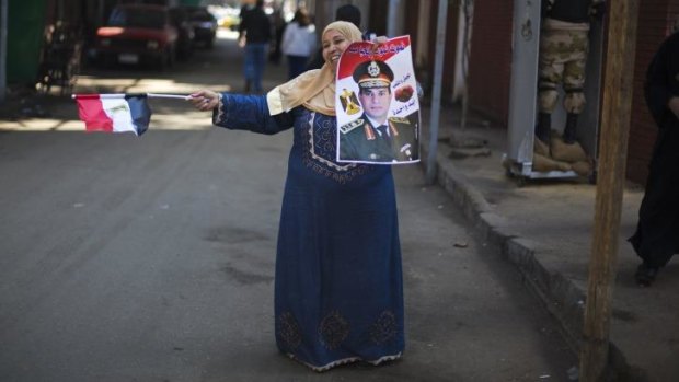 An Egyptian woman dances in front of a polling station holding a poster of General Abdel-Fattah al-Sisi.