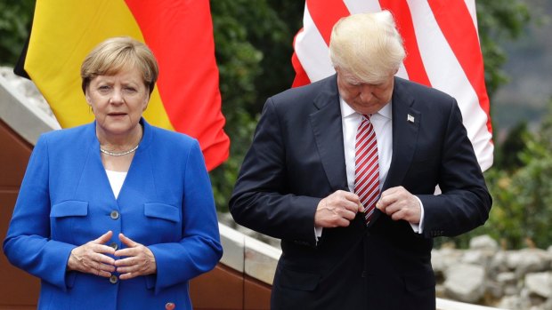Donald Trump adjusts his jacket as he stands with German Chancellor Angela Merkel before a group photo during the G7 summit.