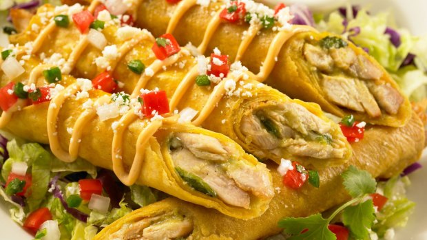 Chicken taquitos served on a bed of lettuce topped with sauce, salsa and cheese.