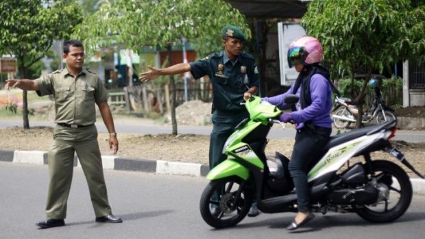 Police officers check a female motorcyclist wearing pants at a checkpoint in Aceh.