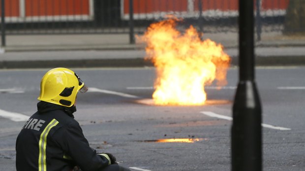 A fireman watches as flames come out of a manhole cover in the road.