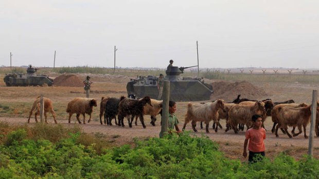 A youth and goats pass by Turkish military stationed on the Turkish side of the border near Syrian rebel-controlled town of Tel Abyad, in Akcakale, Turkey.