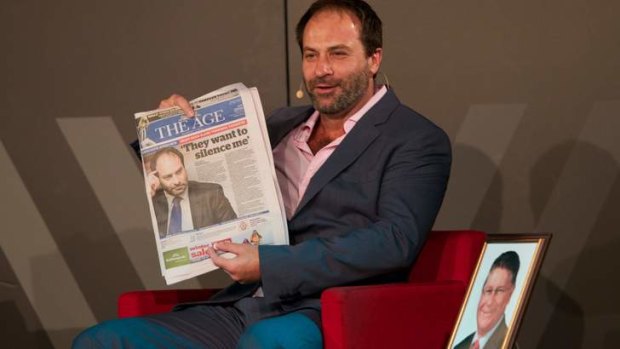 Geoff Shaw holds up a copy of <i>The Age</i> with his photo on the front page while on stage with Sammy J at the Wheeler Centre.