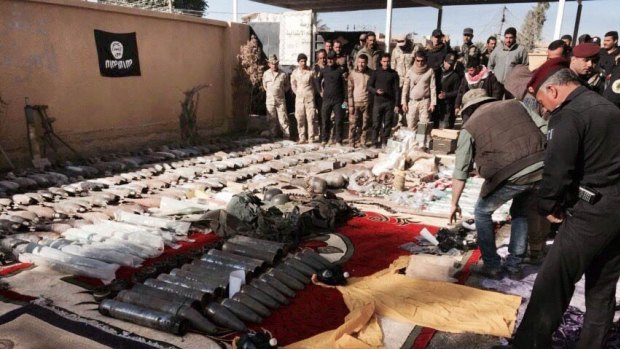 The Iraqi military displays confiscated Islamic State weapons and ammunition, with an IS flag placed upside down in the background as a mark of disrespect.