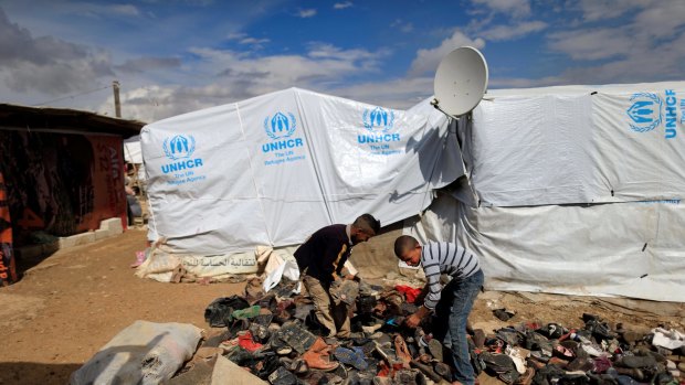 Syrian refugee boys help their family to collect shoes to be added under a fire to boil water outside their family's tent at a refugee camp in Hosh Hareem.