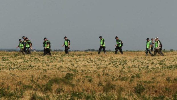 Australian and Dutch police walk across a field during their search last month for remains of victims of MH17.