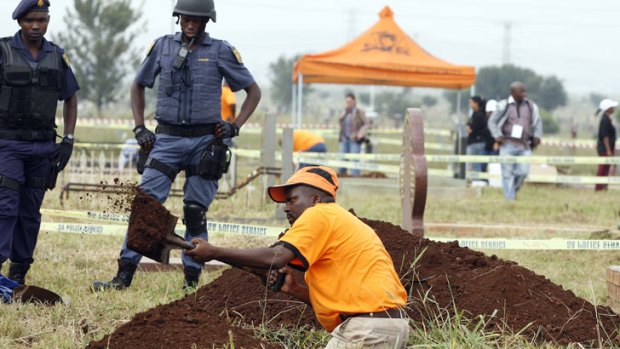 National Prosecuting Authority worker digs up a grave for exhumation of two bodies, that are believed be those of young activists as police officer watch at Avalon Cemetery in Johannesburg, South Africa.