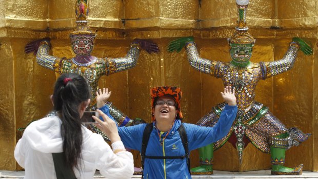 A Chinese tourist strikes a similar pose to statues as they visit the Grand Palace.