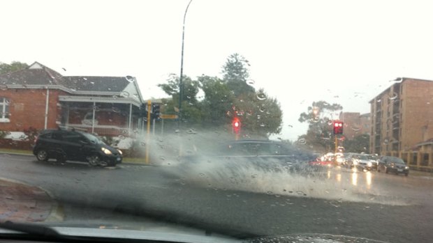 Cars negotiate large pools of water on the road in Leederville this morning.