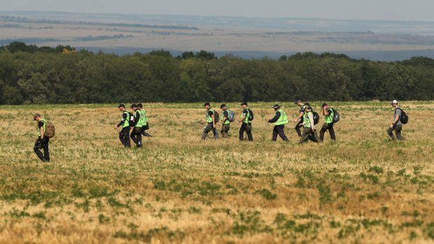 Australian Federal Police and their Dutch counterparts walk across a field searching for remains and personal belongings.