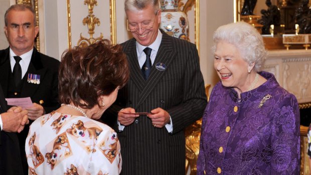 Queen Elizabeth II talks with Kathy Lette, wearing an outfit decorated in corgis wearing crowns.