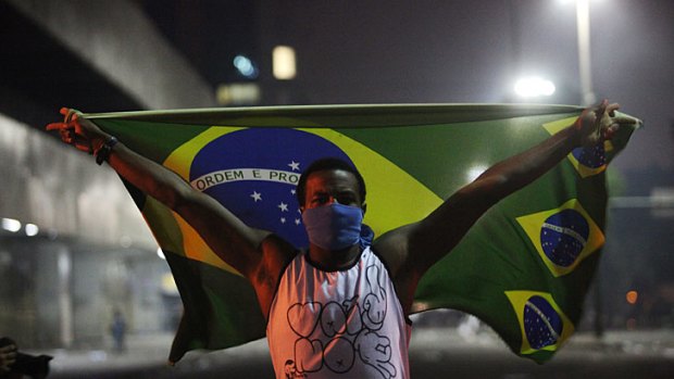 A masked protester holds a Brazilian flag during protests in downtown Rio de Janeiro.