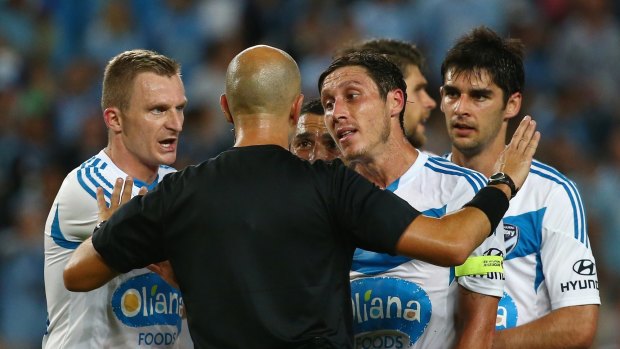 Besart Berisha and Mark Milligan of Melbourne Victory argue with referee Strebre Dilovski after he awarded a penalty.