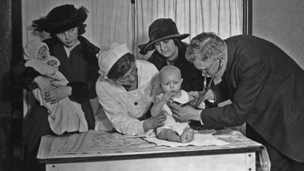 A doctor and a nurse examine a baby, while another mother waits, at a clinic (circa 1915).