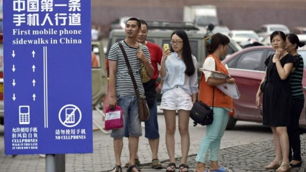 Residents look at a sign with the words "China's First Cellphone Lane" explaining the use of a lane which separates those using their phones as they walk from others in southwest China's Chongqing Municipality.