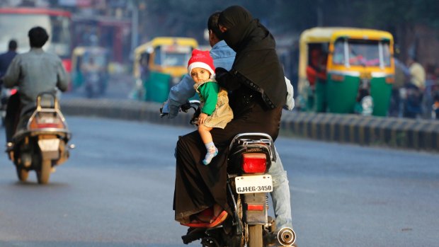 An Indian Muslim woman rides a motorcycle carrying a child wearing a Santa hat in Ahmadabad, India.