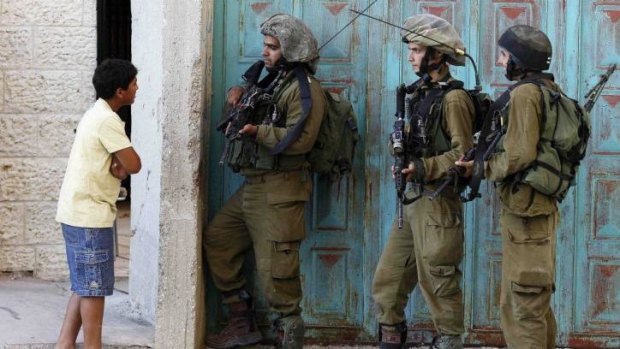 A Palestinian boy speaks to Israeli soldiers in the occupied West Bank city of Hebron during the search for three kidnapped Israeli teenagers.