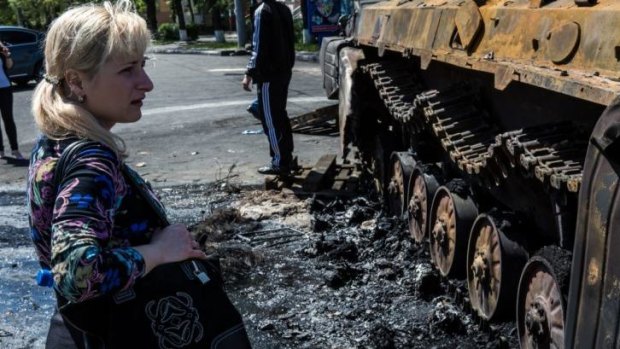 Deadly clashes: a woman looks at a burned Ukrainian government tank on Saturday after fighting in the city of Mariupol.