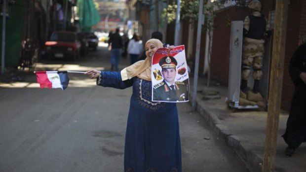 An Egyptian woman dances in front of a polling station holding a poster of Field Marshal Sisi.