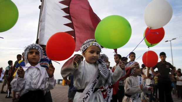 Palestinian children wave colored balloons and Qatari flags.