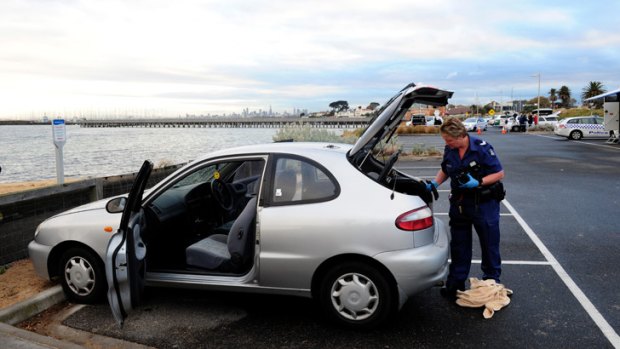 A police forensics officer examines a car parked near the foreshore.