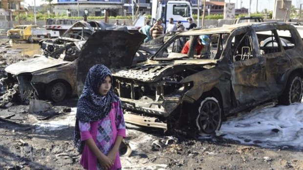 A girl walks past the site of a car bomb attack in Baghdad. A series of bombs targeting restaurants across Baghdad killed at least 21 people on Tuesday.