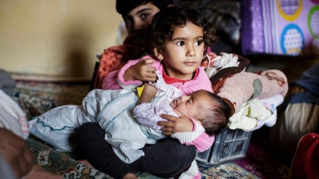 A girl holds a baby in  a family's temporary room in a refugee camp after crossing from Syria into Turkey.