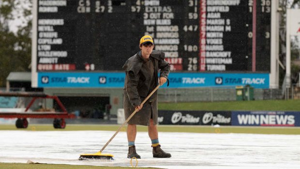 A groundsman sweeps away the rain at Manuka Oval earlier this year.