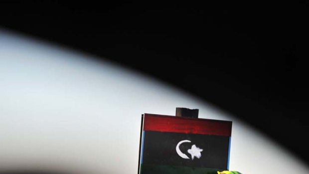 A checkpoint guard paints the Libyan flag on a sign.