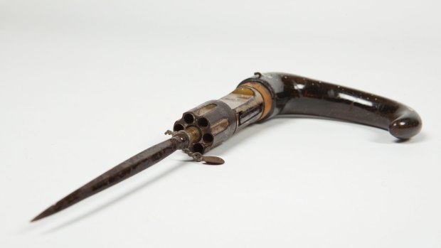 JP1910/419 Six chamber revolver with stiletto, designed to be concealed in a walking stick handle, c1915. Wooden curved handle with revolver and blade attached. Revolver has a folding trigger and is breech loaded. Knife attached to end of revolver has a diamond shaped blade. This object was confiscated by the police from a man named Theodore Mickel (1886-1958) in Wagga Wagga in April 1915. A photograph of the object was published in The Sunday Times 12 September 1920 p.22. Details available in the Vernon Collection Database. Refer to the Registrar, Collections & Access. Theodore Michel six chamber revolver walking stick.?Justice & Police Museum. For Spectrum's objects story.