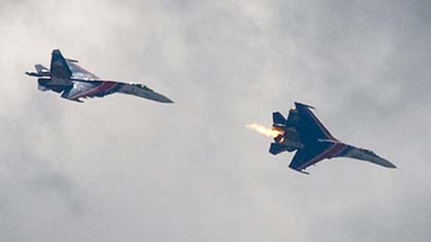An undamaged Su-27 jet, left, follows the burning Su-27, both from the Russian air force elite aerobatic team Russkiye Vityazi (Russian Knights), just seconds after the burning aircraft, right, collided with a two-seat Su-27.