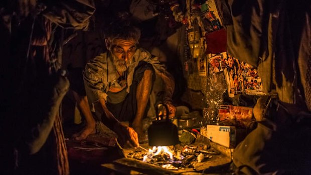 Adam Khan smokes in his cave-like shelter.