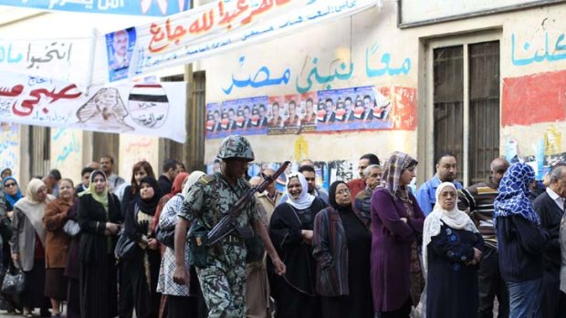 Egyptians wait patiently to cast their vote at a Cairo polling station. On the wall in blue are the words 'all of us together will build Egypt'.