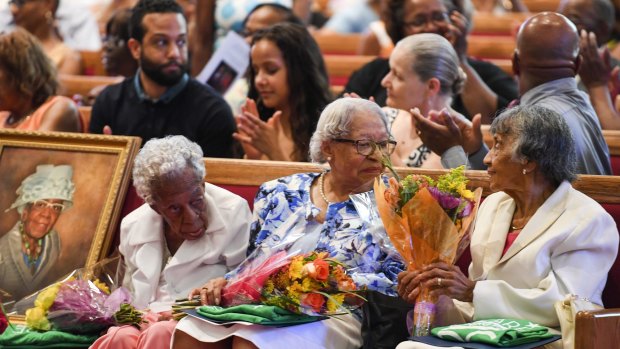 Centenarians (from left) Ruth Chatman Hammett, Gladys Ware Butler and Bernice Grimes Underwood, sitting next to a portrait of their friend Leona Barnes, receive flowers  during their 100th birthday celebration at Zion Baptist Church on Saturday.